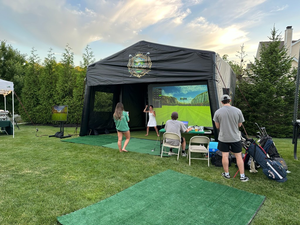 Fore-Play Golf inflatable simulator set up in a backyard at dusk with guests taking swings.