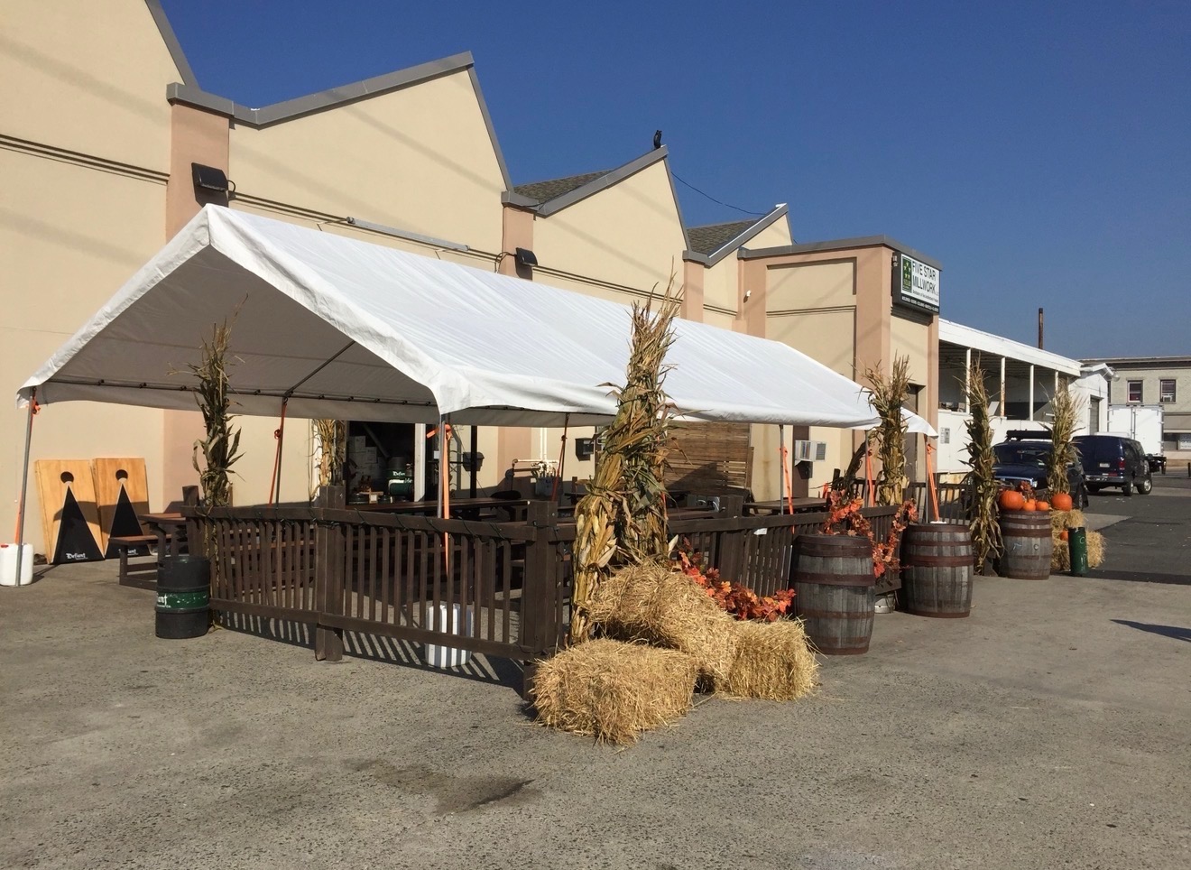 Party tent over patio with picnic tables, hay bales, and autumn decor.
